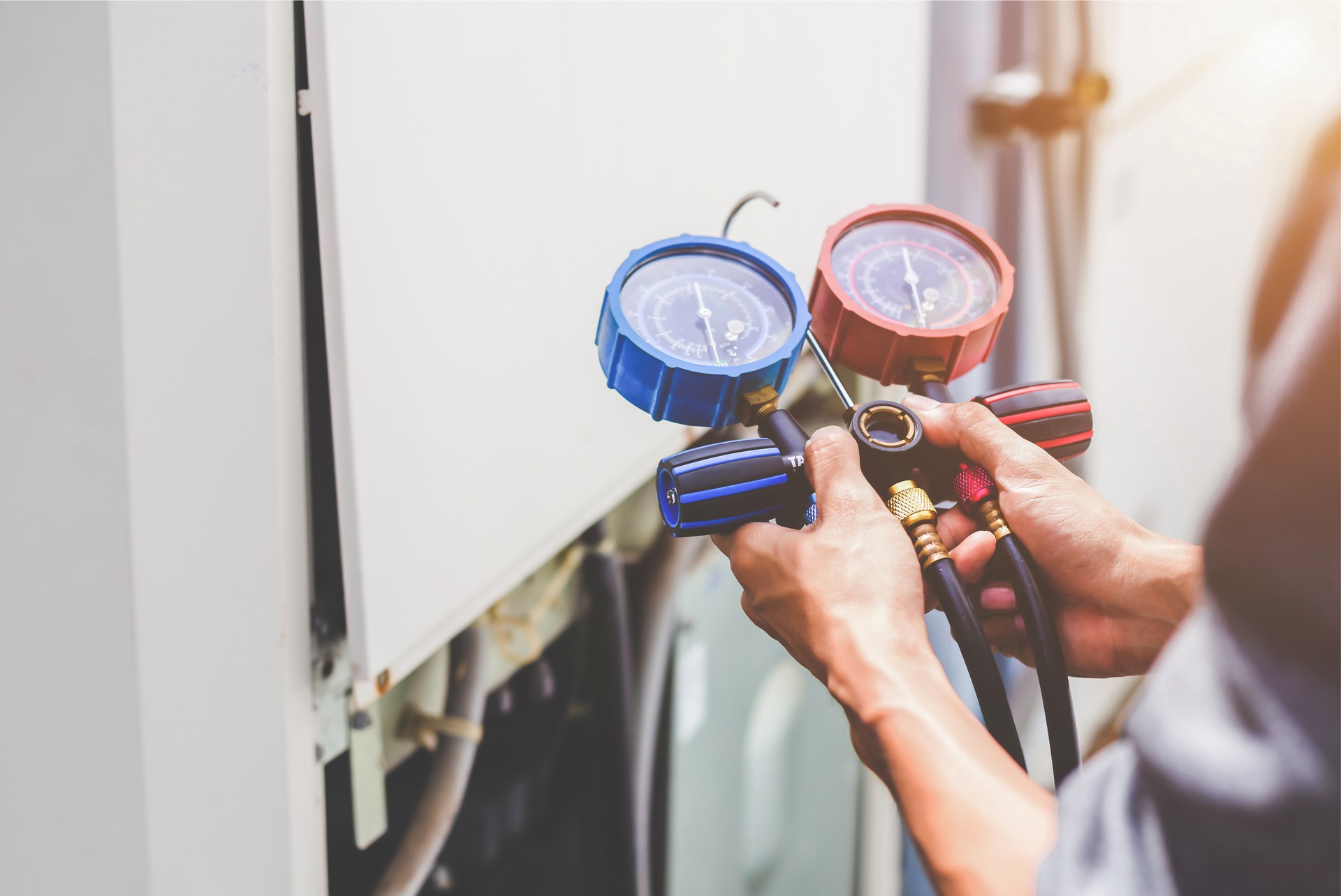 Air repair mechanic using measuring equipment for filling industrial factory air conditioners and checking maintenance outdoor air compressor unit.